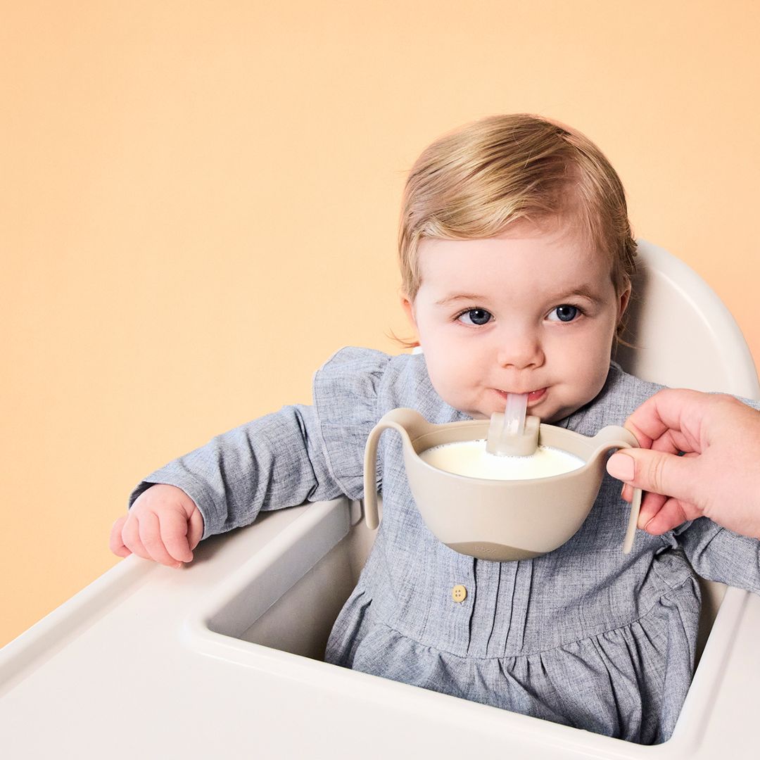 お食事ボウルからストローで牛乳を飲んでいる女の子