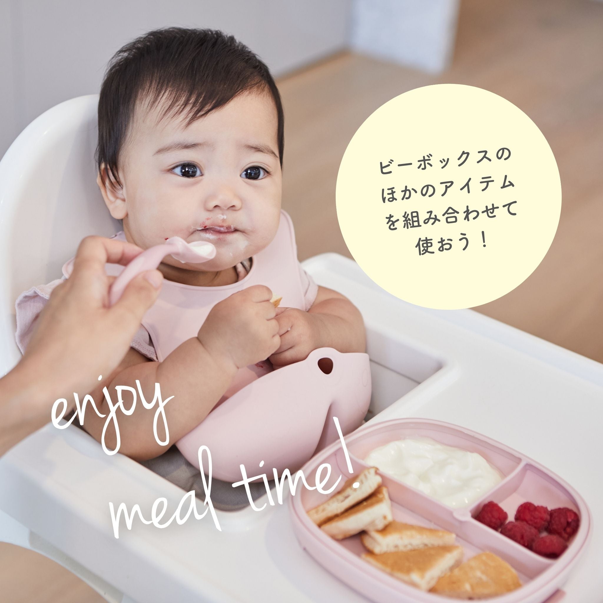 ピンクのスタイを着けた赤ちゃんがハイチェアに座り、スプーンで食事をしている。トレーにはパン、ヨーグルト、ラズベリーがあり、左下に「enjoy meal time!」、右側に「ビーボックスのほかのアイテムを組み合わせて使おう!」のテキストがある。