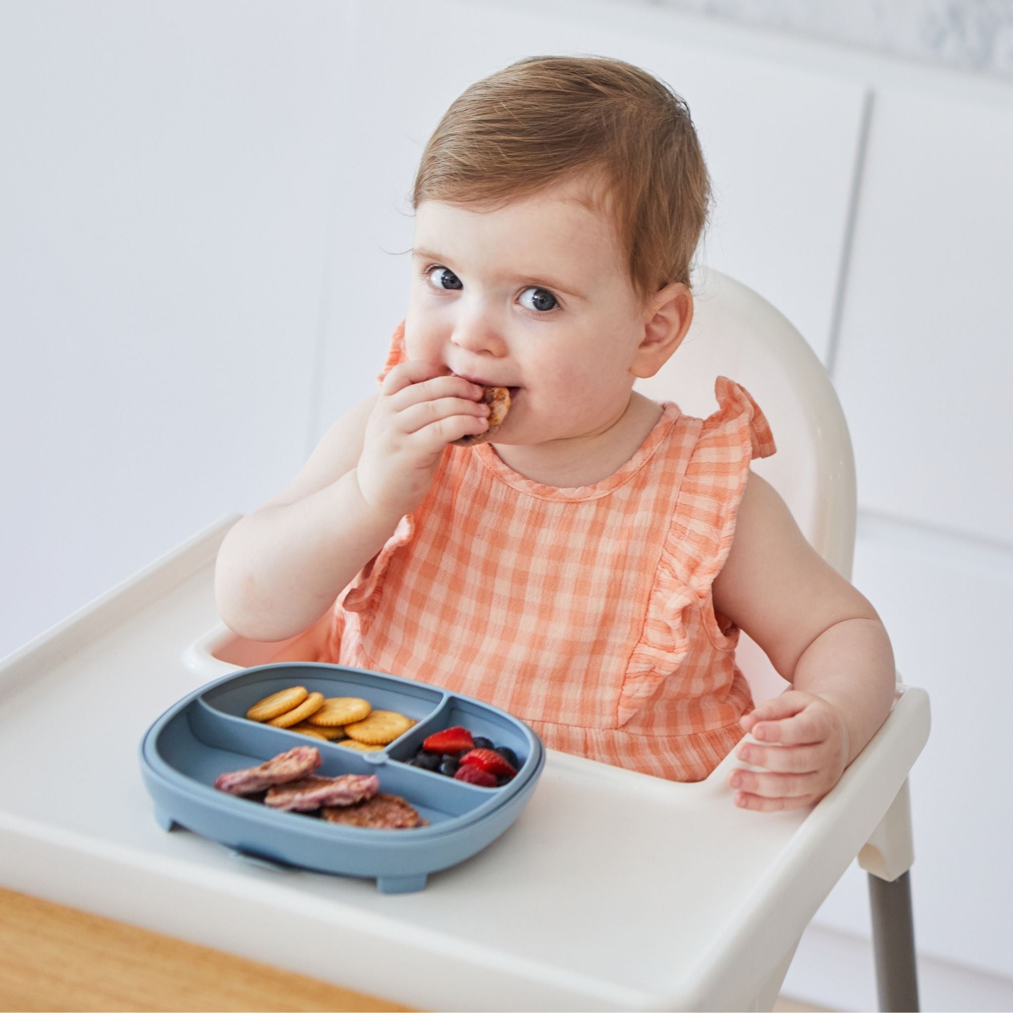 青色の幼児プレートにビスケットとフルーツとおかずが盛り付けてあって女の子がそれを食べている様子