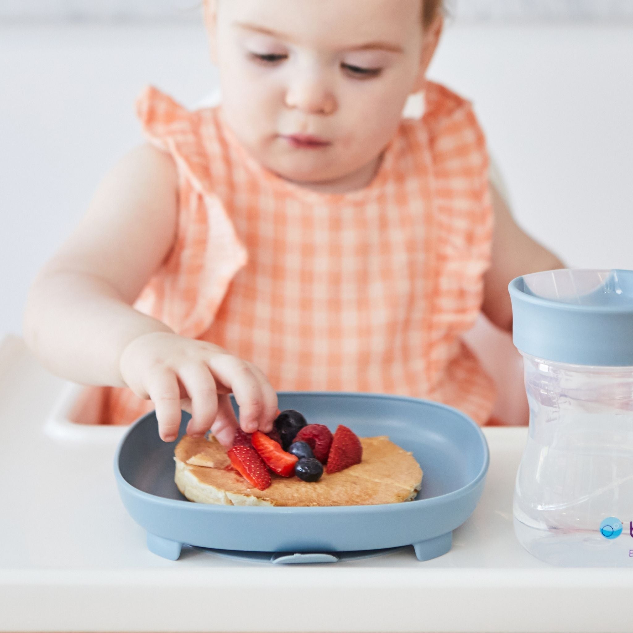 ハイチェアに座った女の子が幼児プレートに盛り付けられたホットケーキを食べている様子