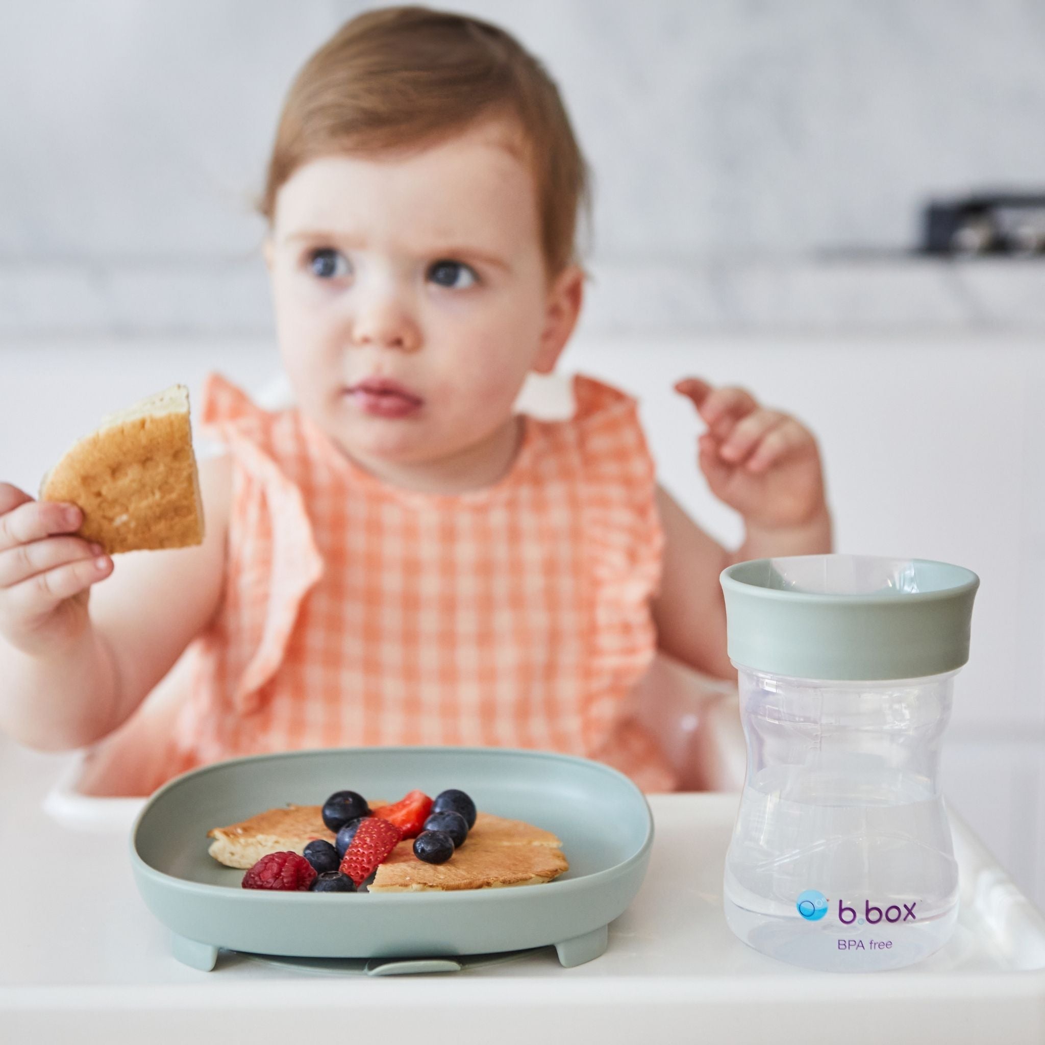 ハイチェアに座った女の子が幼児プレートに盛り付けられたホットケーキを食べている様子