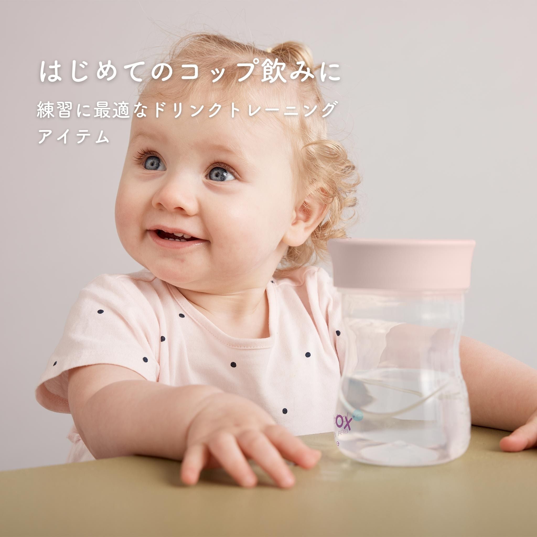 はじめてのコップ飲みに テーブルに置かれたコップ飲みアイテムの後ろに座っている女の子