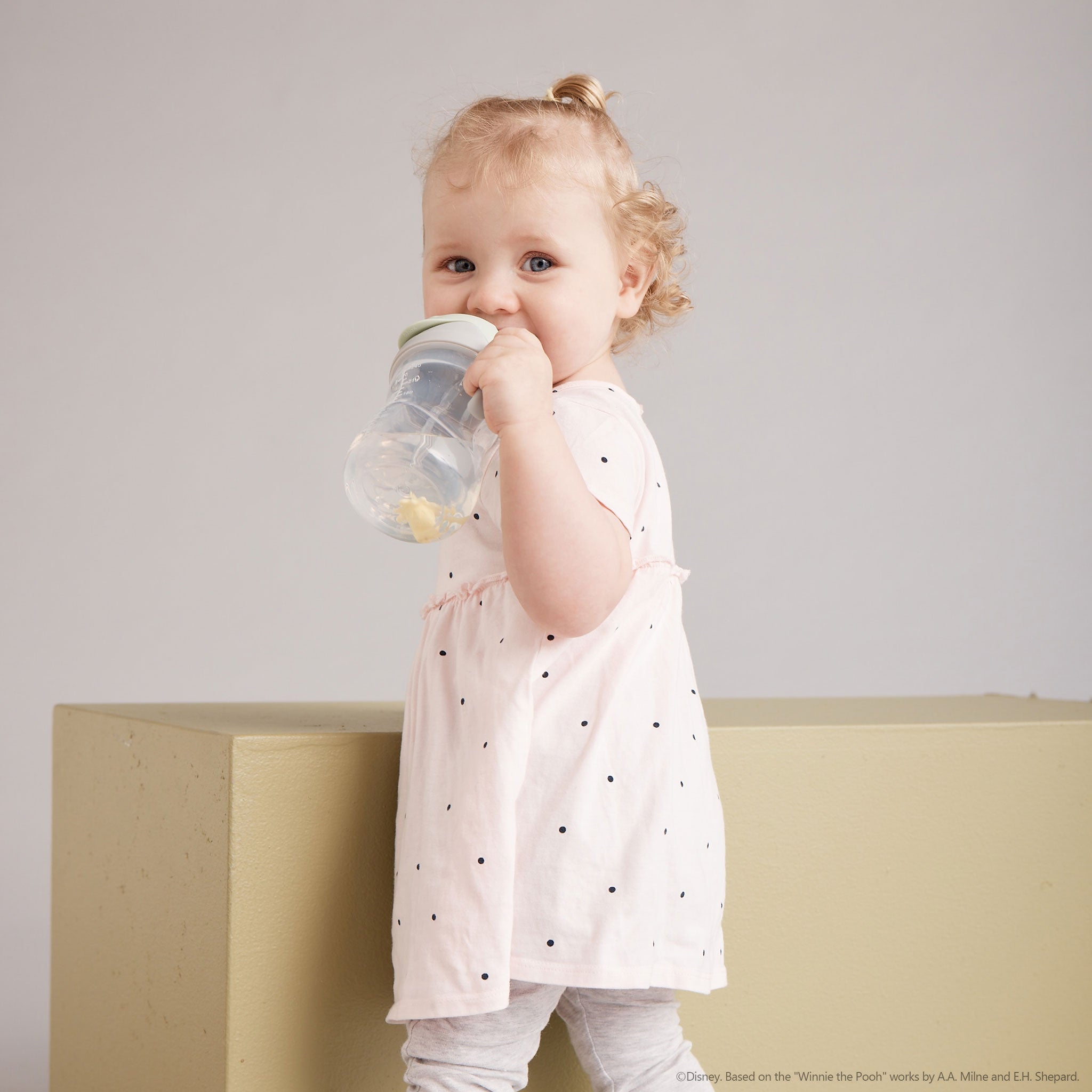 人気のシッピーカップくまのプーさんデザインを持って飲んでいる女の子の赤ちゃん