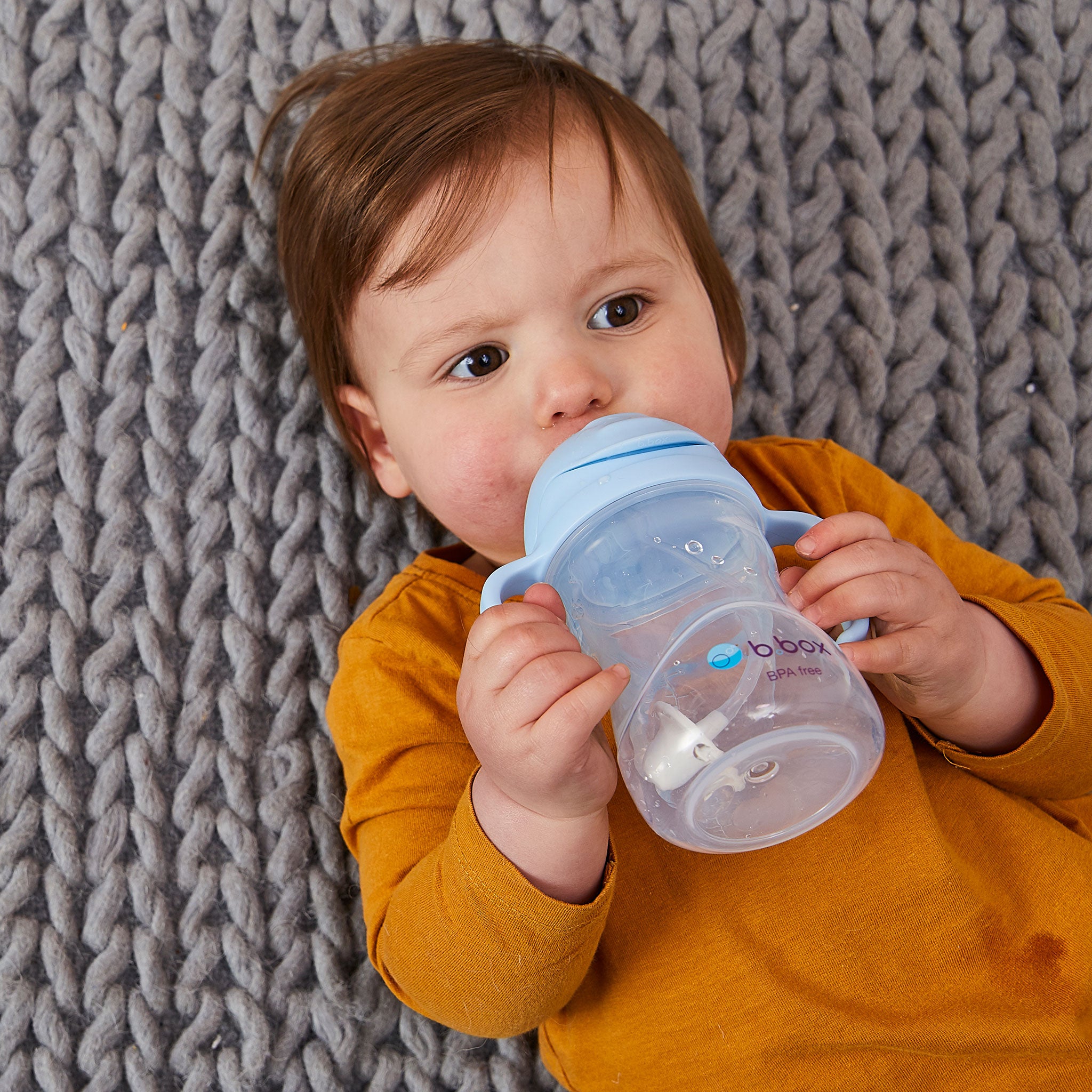 寝転がってシッピーカップを飲む男の子