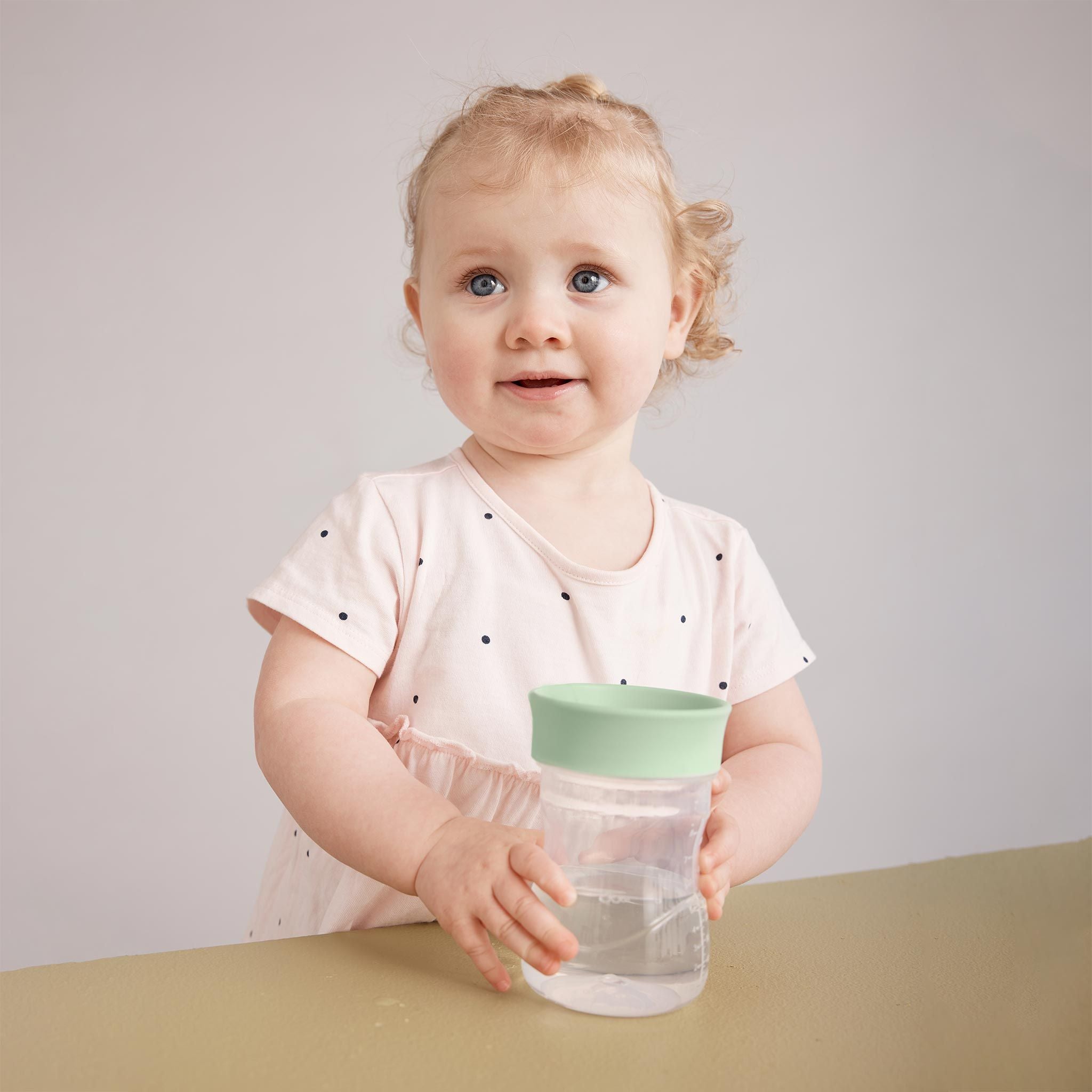 緑色の蓋の付いたコップ飲みアイテムを持つ女の子の赤ちゃんの様子